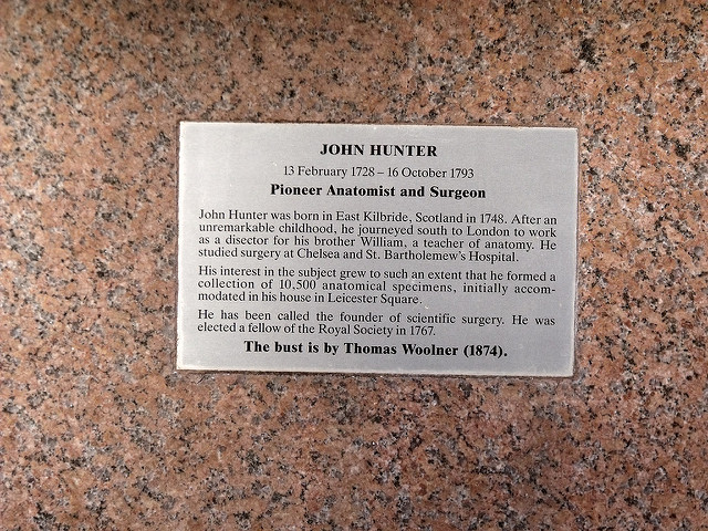 John Hunter brass plaque - John Hunter, 13 February 1728 - 16 October 1793, Pioneer Anatomist and Surgeon.    John Hunter was born in East Kilbride, Scotland in 1728. After an unremarkable childhood, he journeyed south to London to work as a disector {sic} for his brother William, a teacher of anatomy. He studied surgery at Chelsea and St. Bartholemew's {sic} Hospital.    His interest in the subject grew to such an extent that he formed a collection of 10,500 anatomical specimens, initially accommodated in his house in Le