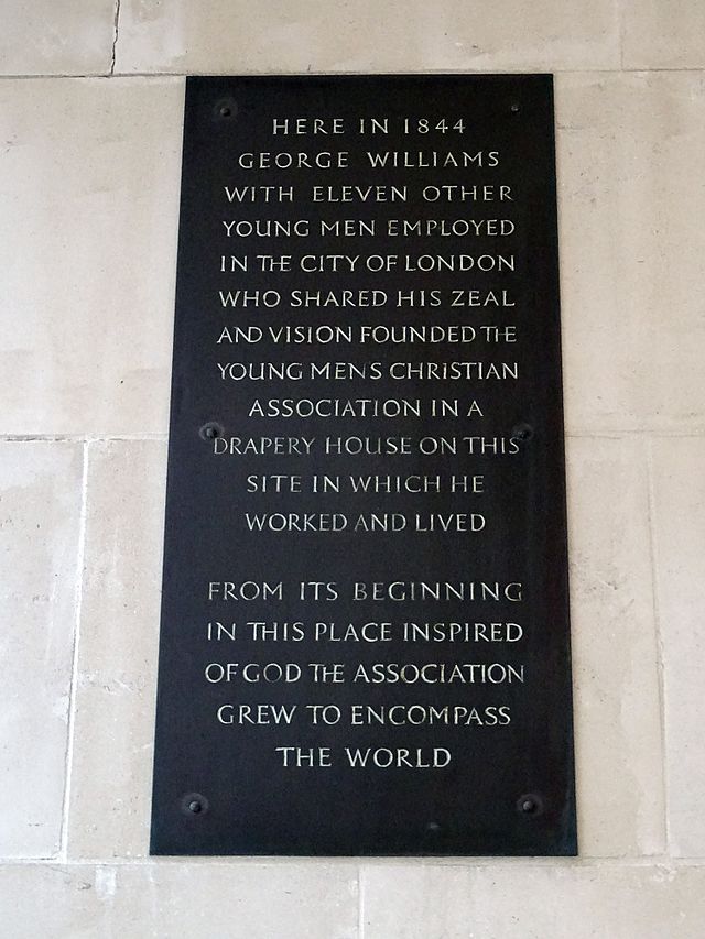 George Williams and Young Men's Christian Association black plaque - Here in 1844 George Williams with eleven other young men employed in the City of London who shared his zeal and vision founded the Young Men's Christian Association in a drapery house on this site in which he worked and lived.  From its beginning in this place inspired of God the Association grew to encompass the world.