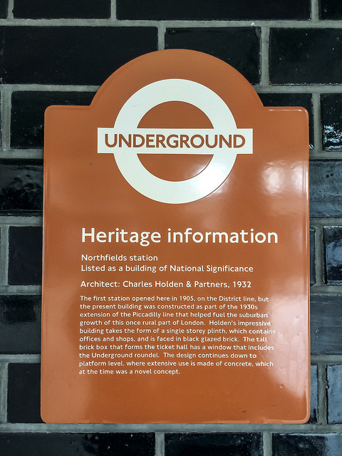 Charles Holden brown plaque - Northfields Station  Architect: Charles Holden & Partners, 1932  The first station opened here in 1905, on the District line, but the present building was constructed as part of the 1930's extension of the Piccadilly line that helped fuel the suburban growth of this once rural part of London.  Holden's impressive building takes the form of a single storey plinth, which contains offices and shops, and is faced in black glazed brick.  The tall brick box that forms the ticket hall has a window that